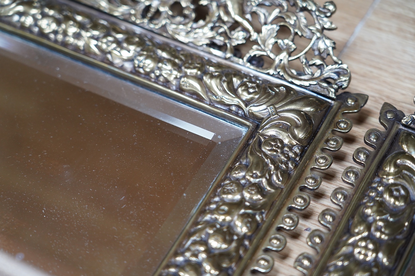 A pair of French brass repoussé mirrors with an ornate putti top and mask decorated bottom, 49cm high. Condition - good